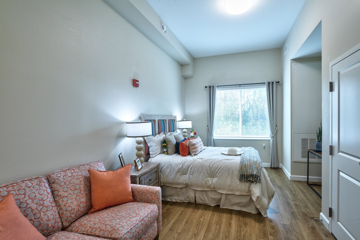A cozy bedroom with a bed, two lamps, and a window providing natural light.