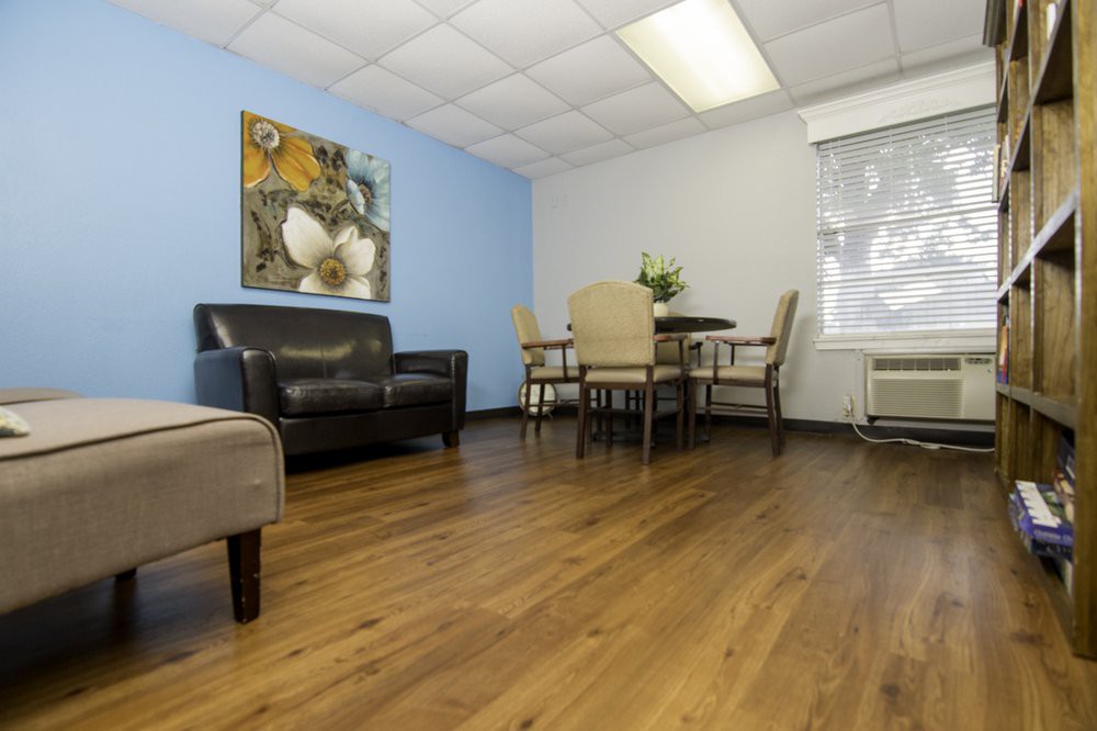A cozy waiting room with a sofa, table, and chairs, adorned with artwork on the wall.