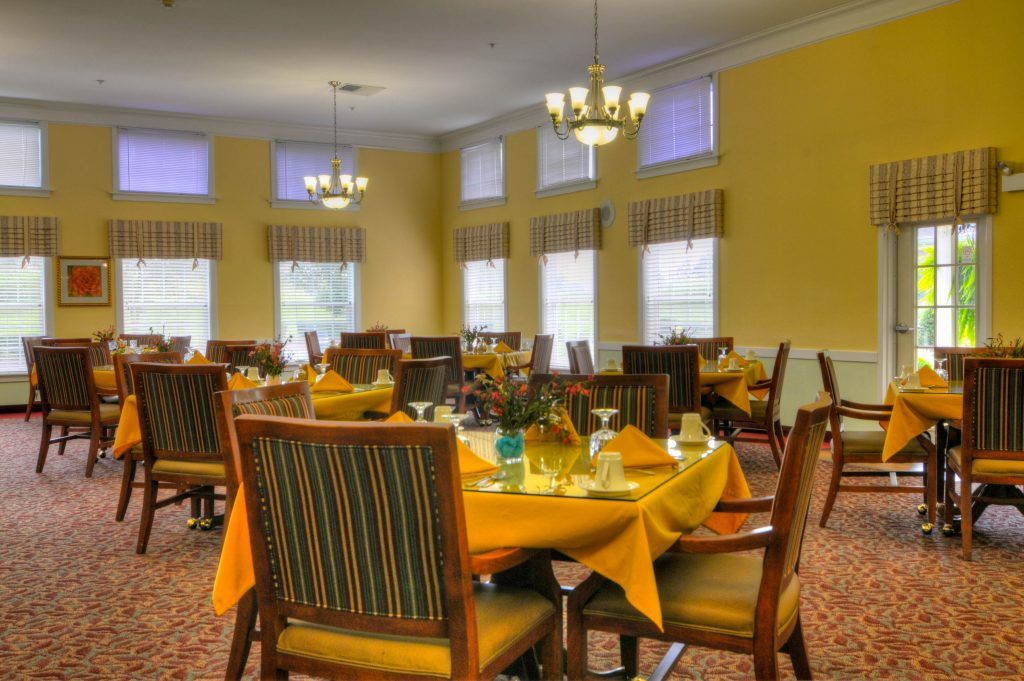 A well-lit dining room with neatly set tables and elegant chandeliers.