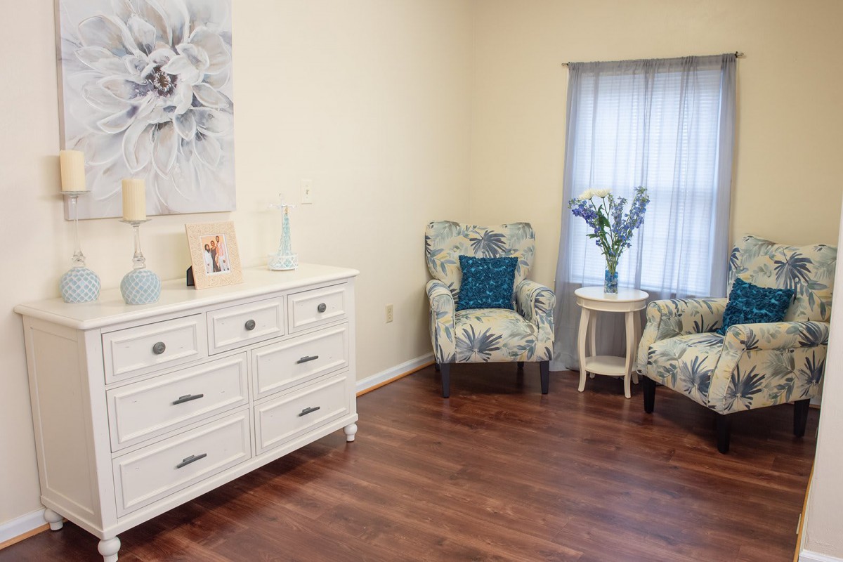 A cozy living room with floral armchairs, a white dresser, and hardwood flooring.