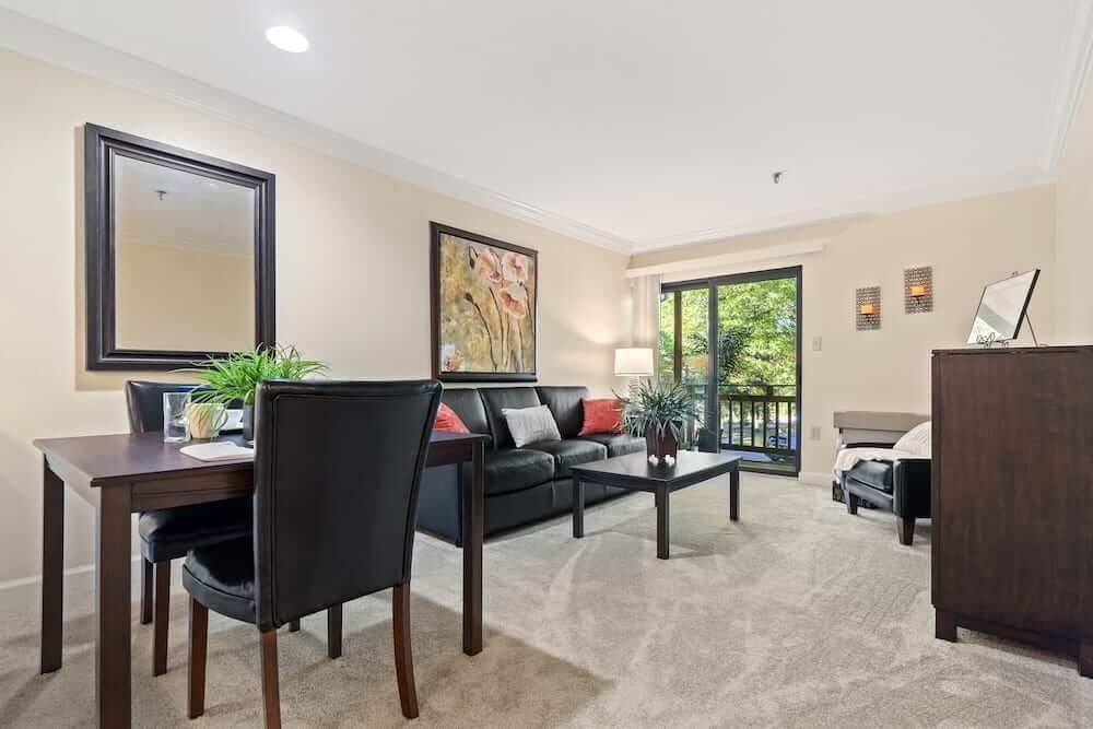 A cozy and well-decorated living room with a sofa, coffee table, dining area, and large windows.