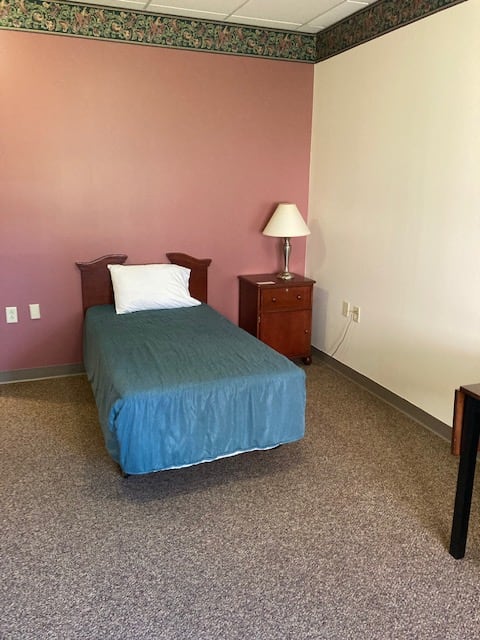 A minimalist bedroom with a single bed and a nightstand with a lamp.