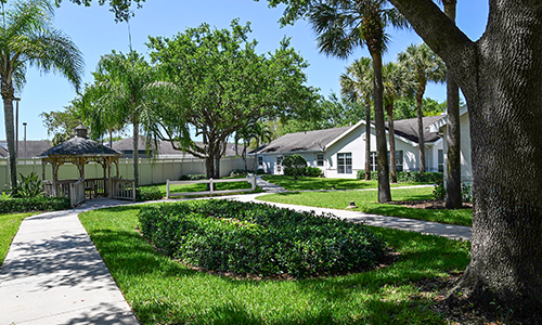 A picturesque residential area featuring lush green lawns, trees, and a pathway leading to charming houses.