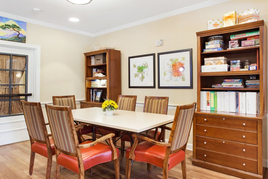 A well-furnished dining or meeting room with a table, chairs, bookshelves, and artwork on the wall.