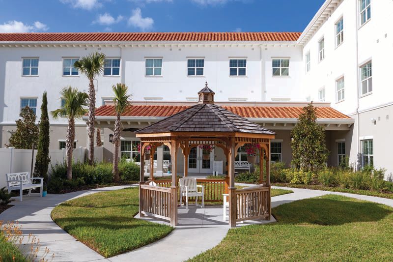 A picturesque gazebo nestled in a landscaped garden with pathways and surrounded by a building.