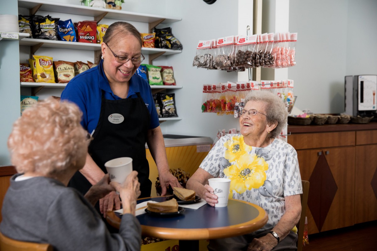 A friendly interaction in a cafe between staff and elderly patrons.