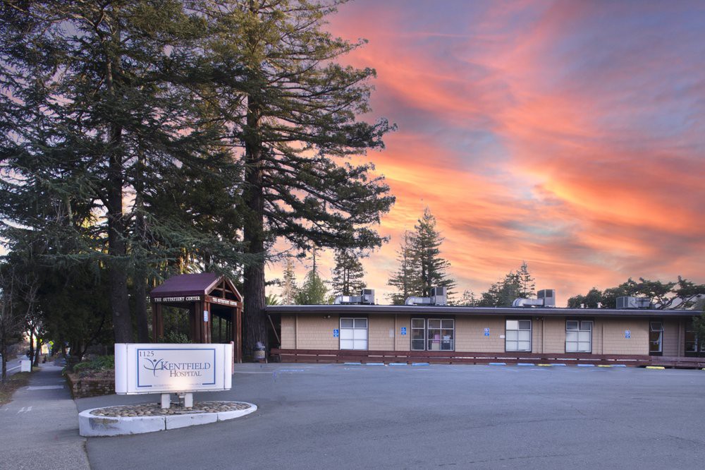 A school building with a beautiful sunset sky in the background, surrounded by tall trees.