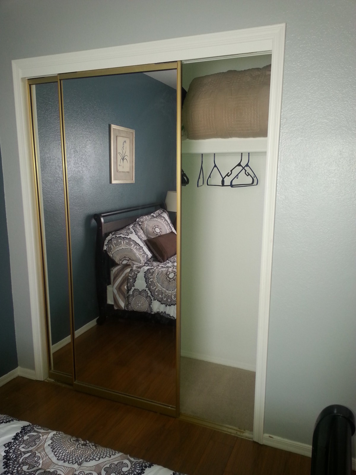 A bedroom with mirrored closet doors revealing an interior containing blankets and hangers.