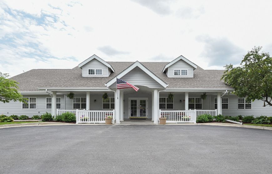 A white house with a porch and an American flag flying outside, set against a cloudy sky.