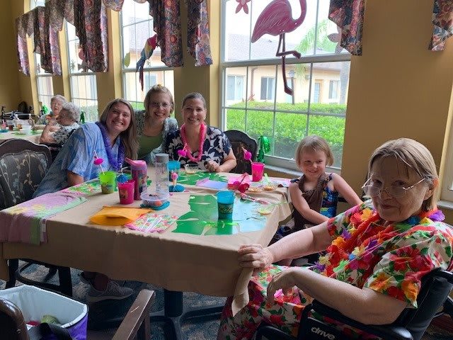 A group of people enjoying a gathering indoors, seated around a table with crafts and decorations.