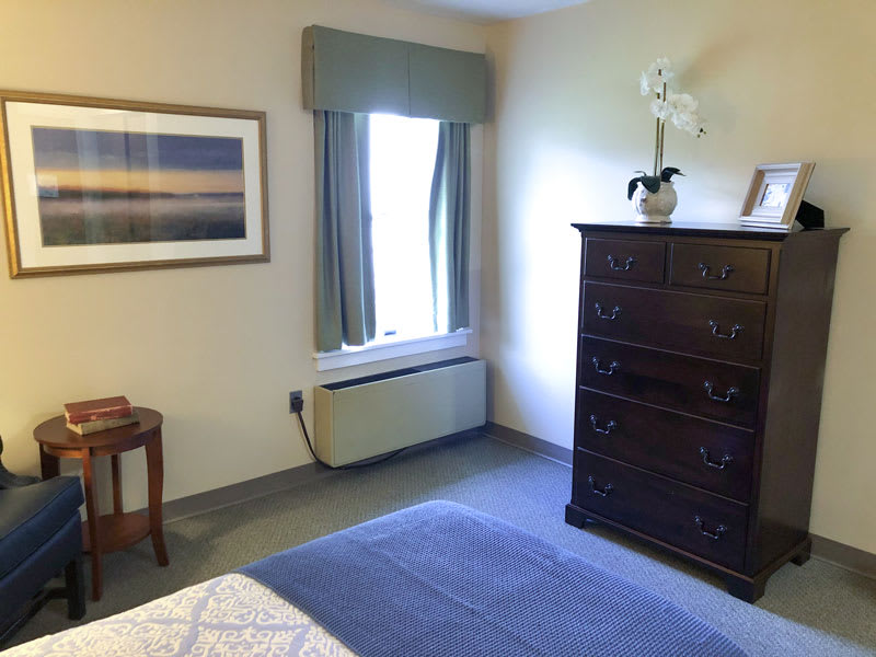 A cozy bedroom with a tall dresser, a window with curtains, and a painting on the wall.