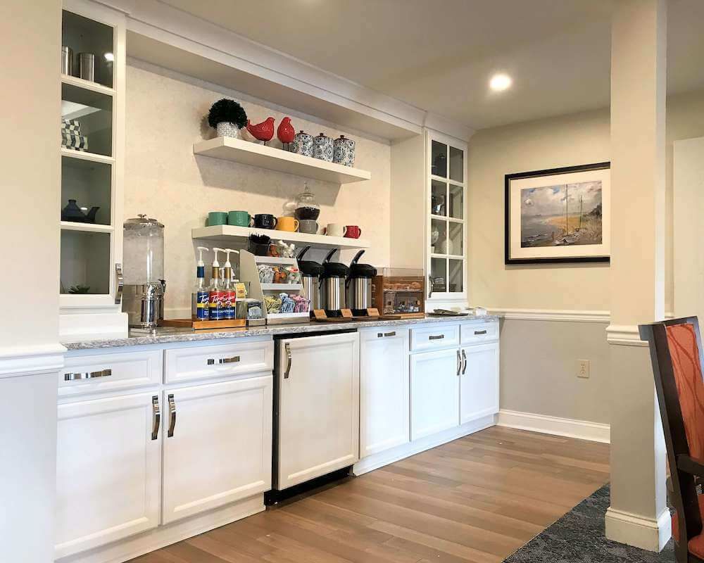 A modern kitchen area with white cabinets and a coffee station.