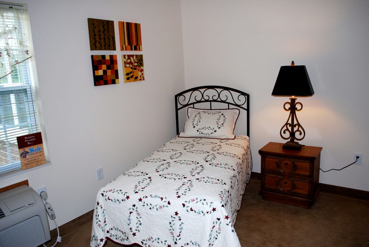 A cozy bedroom with a single bed, decorative pillows, and a nightstand with a lamp.