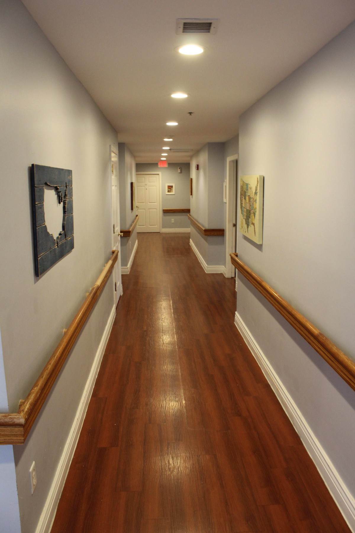 A long hallway with artwork and wooden floors, typical of a hospital or nursing home.