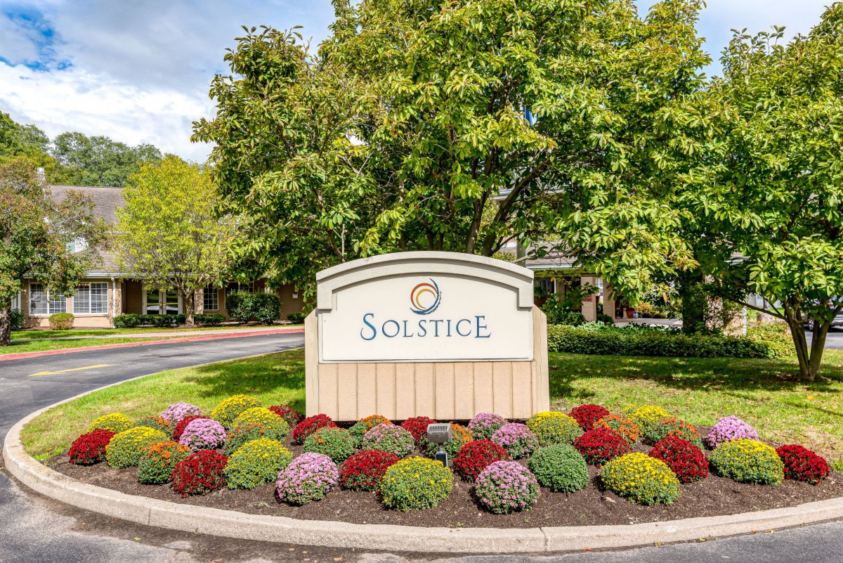 Entrance sign of Solstice surrounded by colorful flowers and greenery.