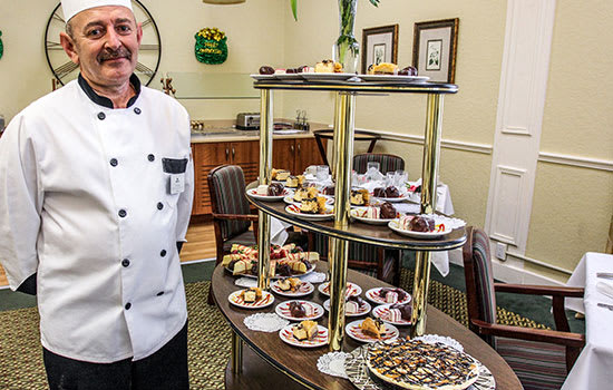 A chef standing beside a buffet table filled with an assortment of desserts and pastries.