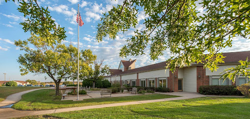 A beautiful view of a building surrounded by lush greenery and under a partly cloudy sky, featuring an American flag.