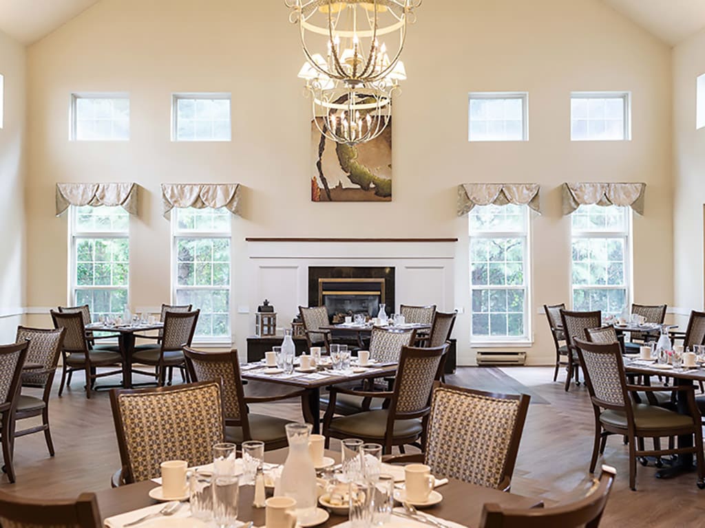 An elegant dining room setup with multiple tables, a chandelier, and a fireplace.