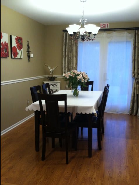 A cozy dining room with a table set for four, featuring a chandelier and flower centerpiece.