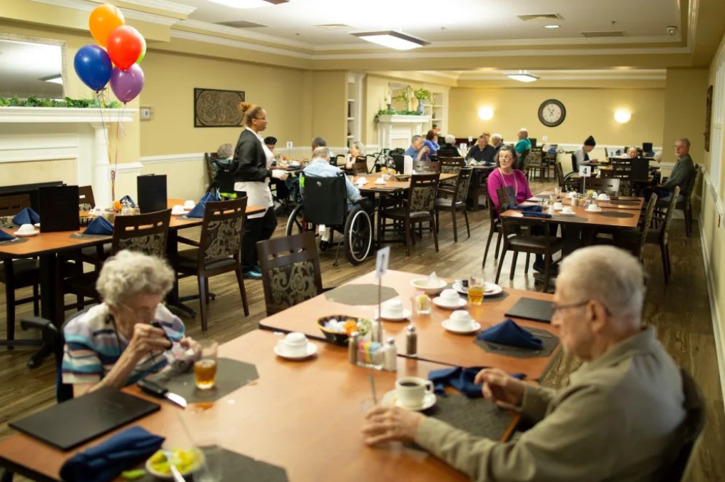 Elderly individuals enjoying a meal together in a nursing home dining room.