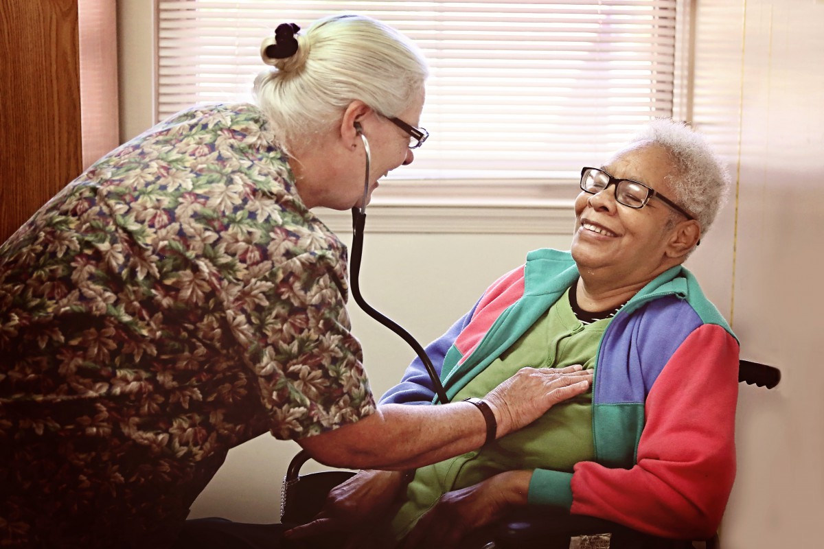 A healthcare professional conducts a medical examination on a smiling patient using a stethoscope.