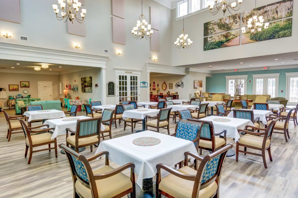 A spacious and well-lit dining room with neatly arranged tables and chairs, adorned with elegant chandeliers.
