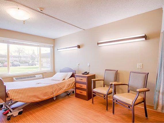 An empty hospital room with a bed, two chairs, and a window, creating a clean and quiet atmosphere.