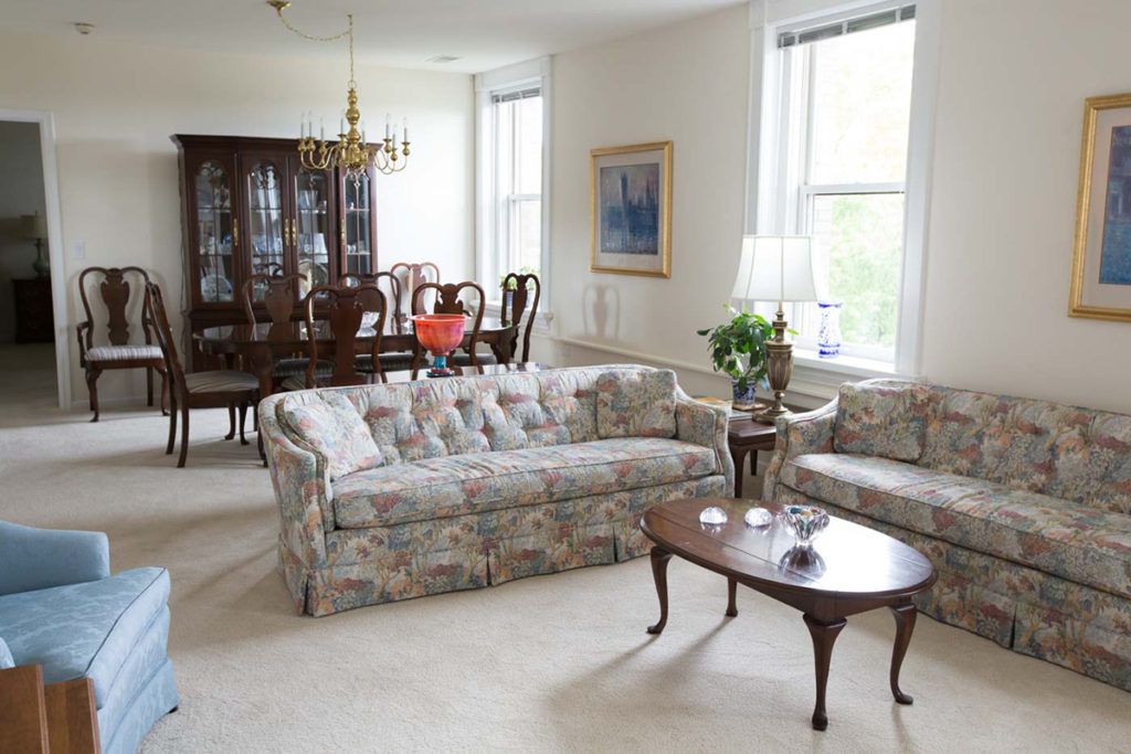A bright living and dining area featuring a floral sofa set and a wooden dining table with chairs.