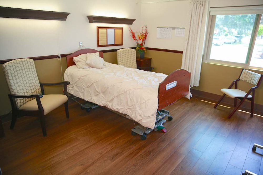 A clean and minimalistic hospital room with a single bed and wooden flooring.