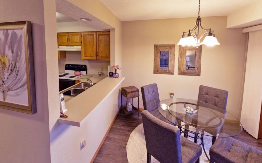 A cozy dining area with a glass table and cushioned chairs adjacent to a kitchen space.