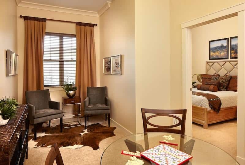 A cozy living area featuring a seating space with two armchairs, a glass table set for board games, and decorative artwork on the wall.