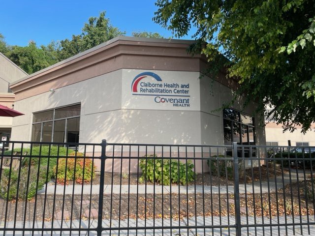 A building with a sign reading 'California Driver and Safety Education Center' behind a fence and surrounded by trees.