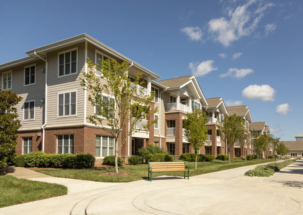 A modern apartment building with well-maintained landscaping and a nearby bench on a sunny day.