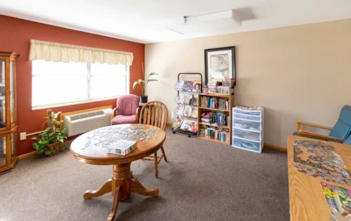 A cozy room featuring a round table, bookshelf, and a comfortable chair by the window.