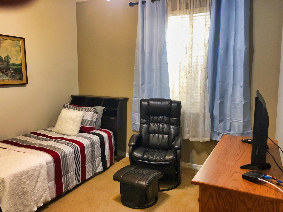 A cozy bedroom with a single bed, black reclining chair, and wooden desk.