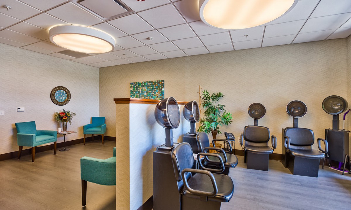 A modern salon interior featuring chairs with hair dryers, a waiting area, and plants.