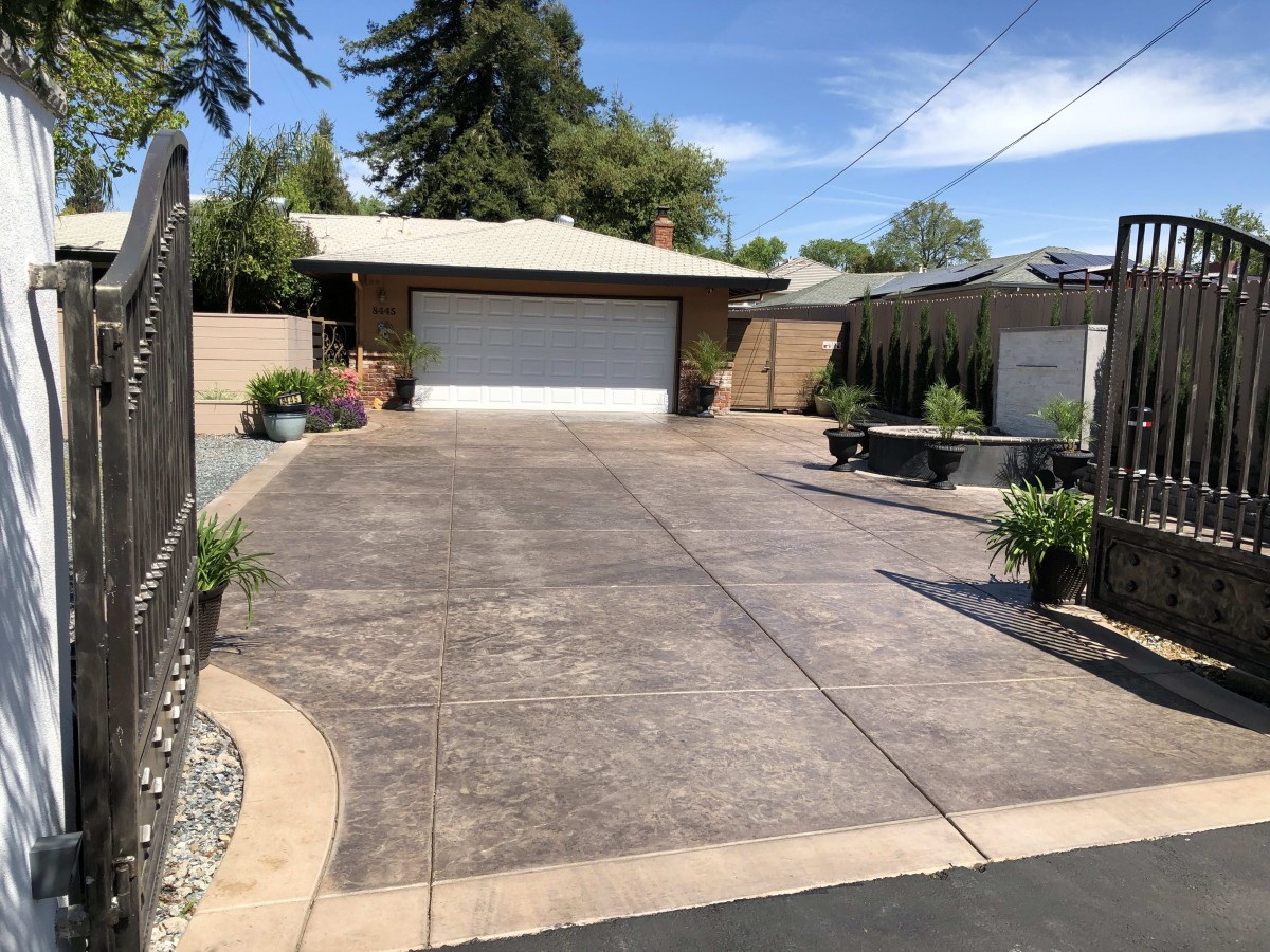 A residential house with a paved driveway and garage, surrounded by trees under a clear sky.