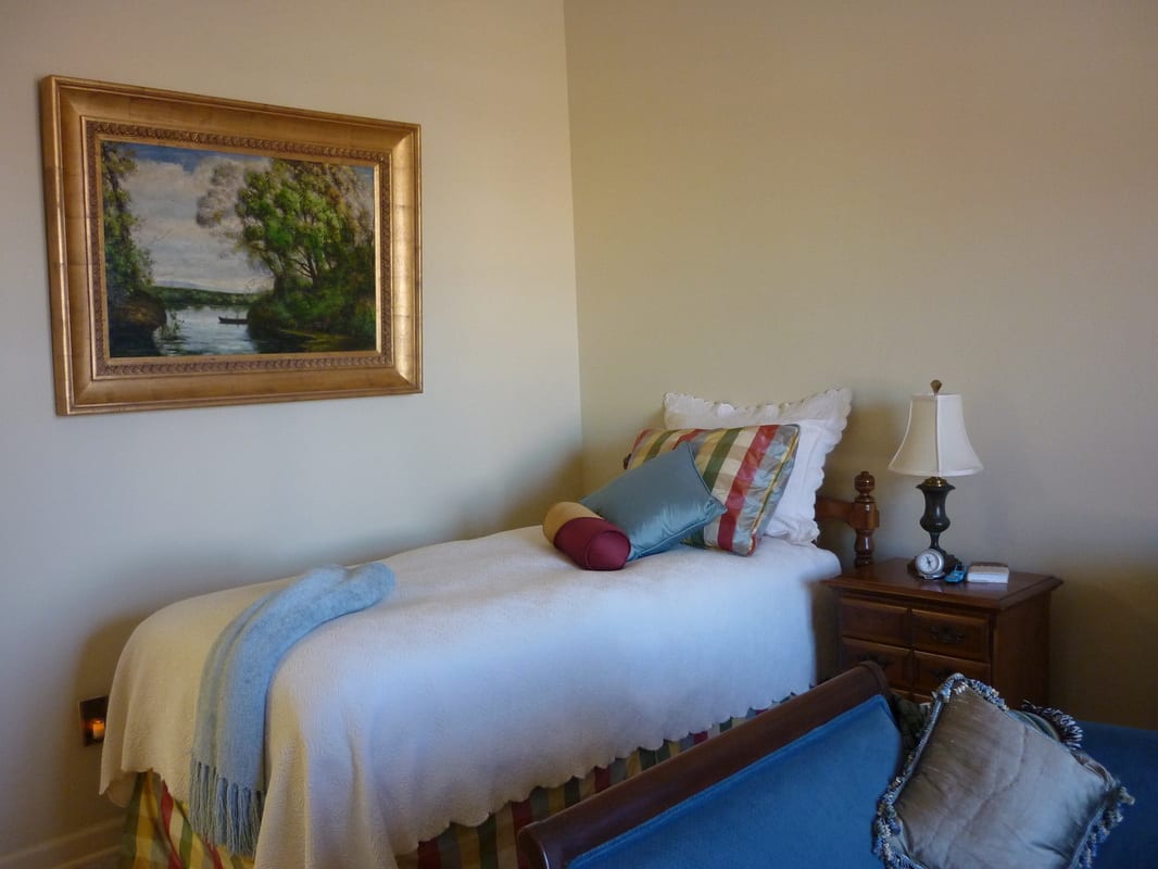 A cozy bedroom with a single bed, colorful pillows, and a painting on the wall.