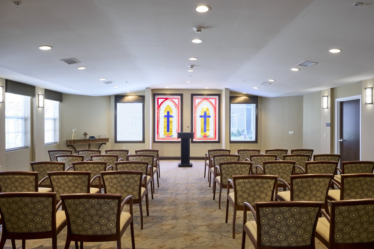 An empty chapel with rows of chairs and stained glass windows.