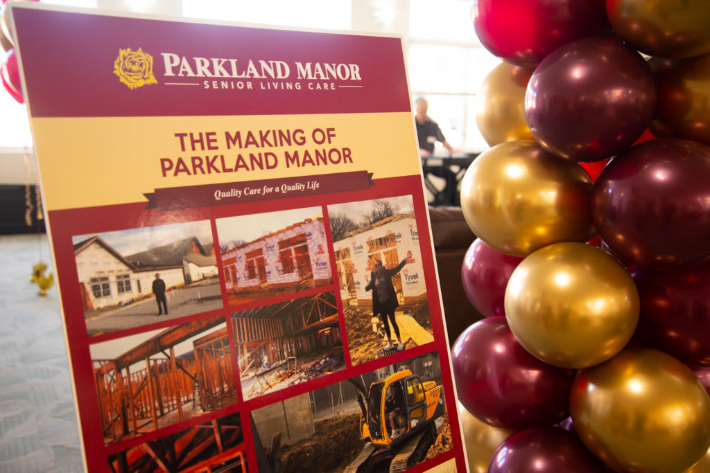 A display sign at an event for Parkland Manor features photographs of its construction, accompanied by festive balloons.