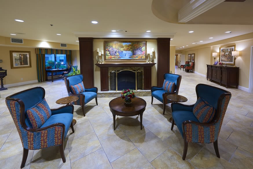 A cozy lounge area with comfortable chairs arranged around a central coffee table in front of a fireplace, decorated with artwork above.