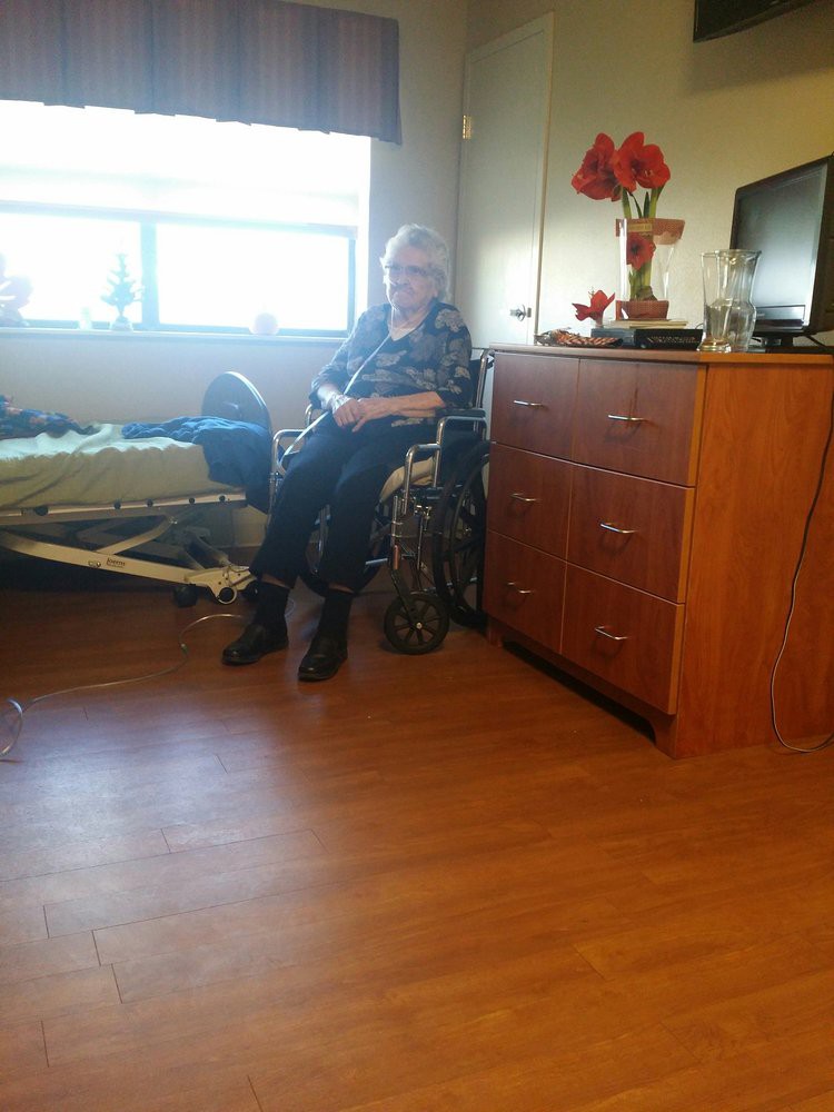 An elderly person in a wheelchair sitting in a nursing home room.