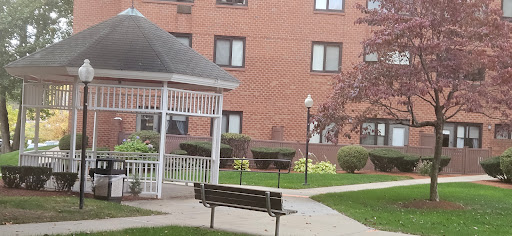 A peaceful outdoor area featuring a bench and gazebo near an apartment building.