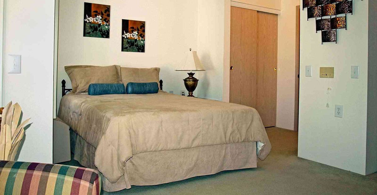 A cozy bedroom with a neatly made bed, bedside lamp, and decorative artwork on the wall.