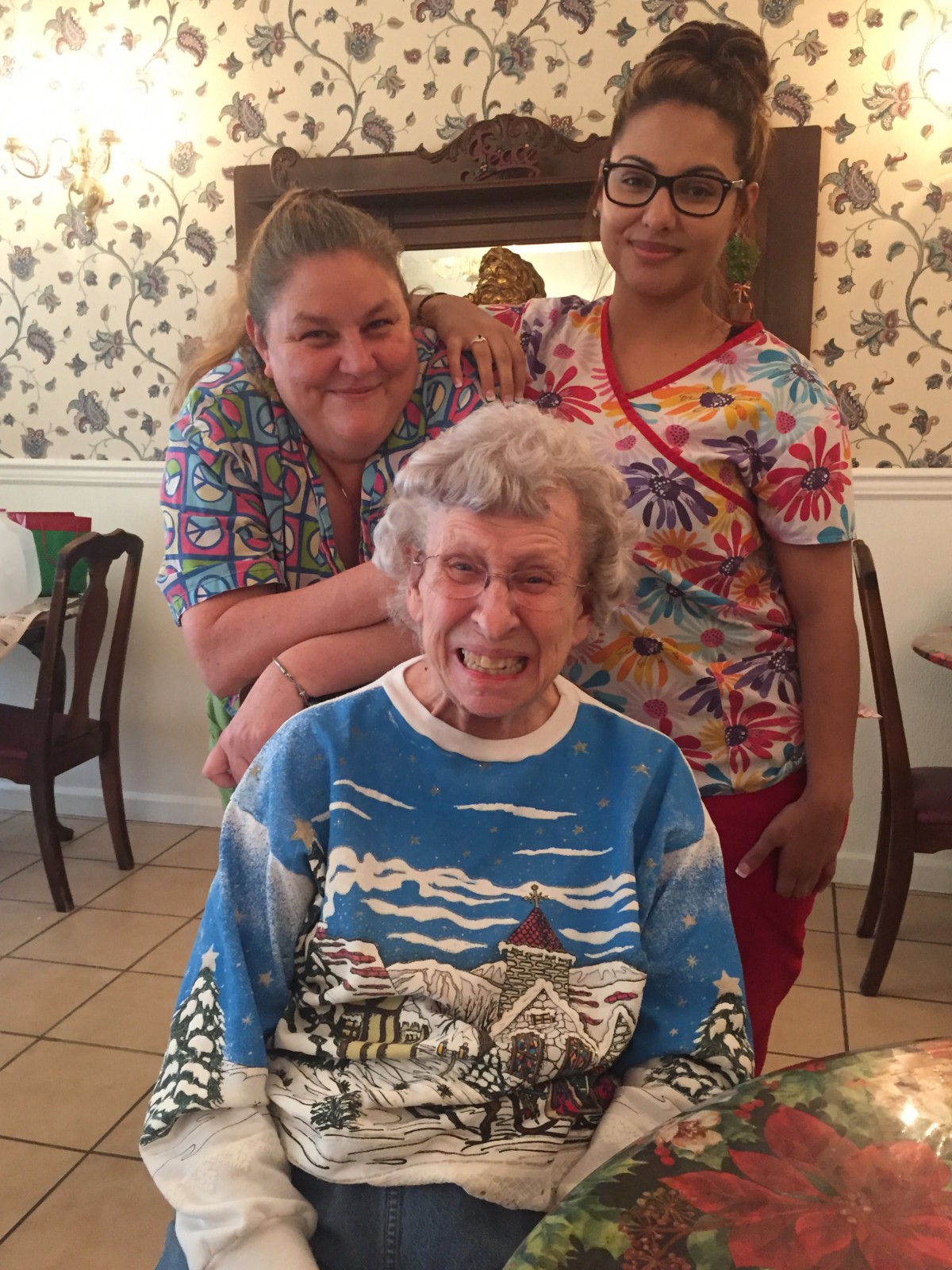 A joyful multigenerational family gathering, featuring an elderly woman seated with two smiling women standing behind her.