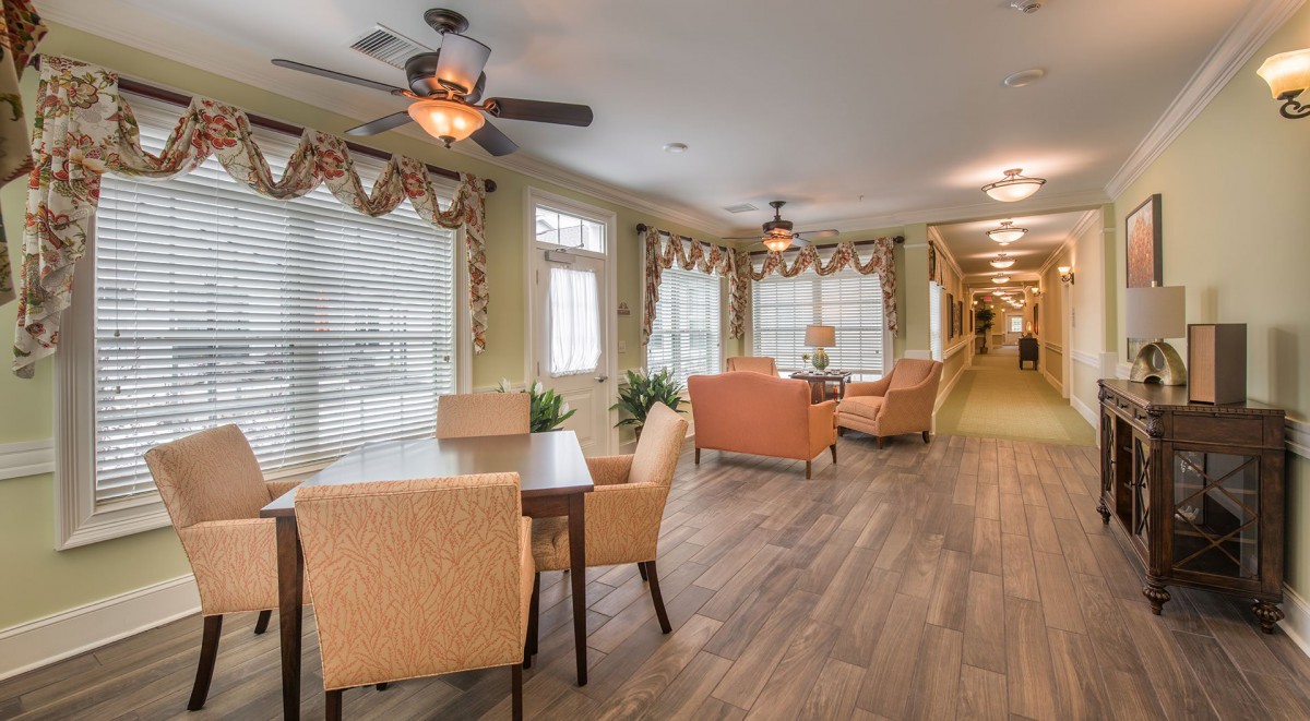 A cozy seating area with comfortable chairs and tables, well-lit by large windows and enhanced with wooden flooring and ceiling fans.