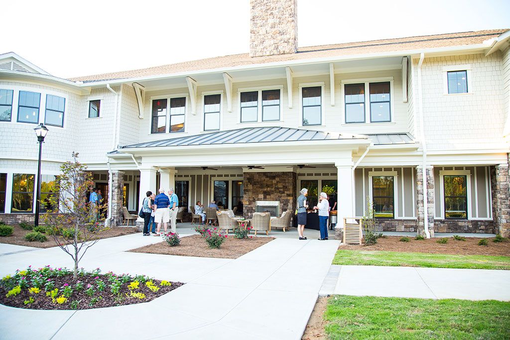 A group of people gathering outside a large house with a spacious patio and well-kept lawn.