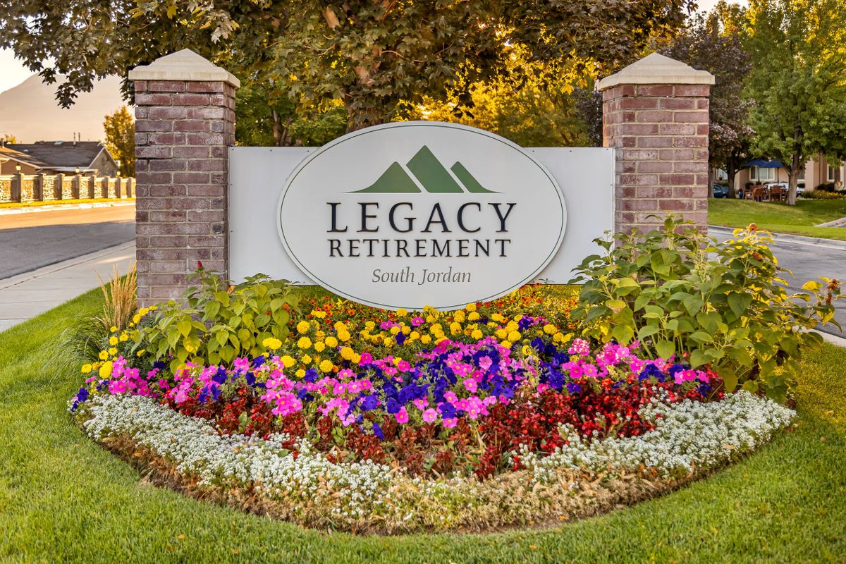 Entrance sign to Legacy Retirement surrounded by colorful flowers and landscaping.