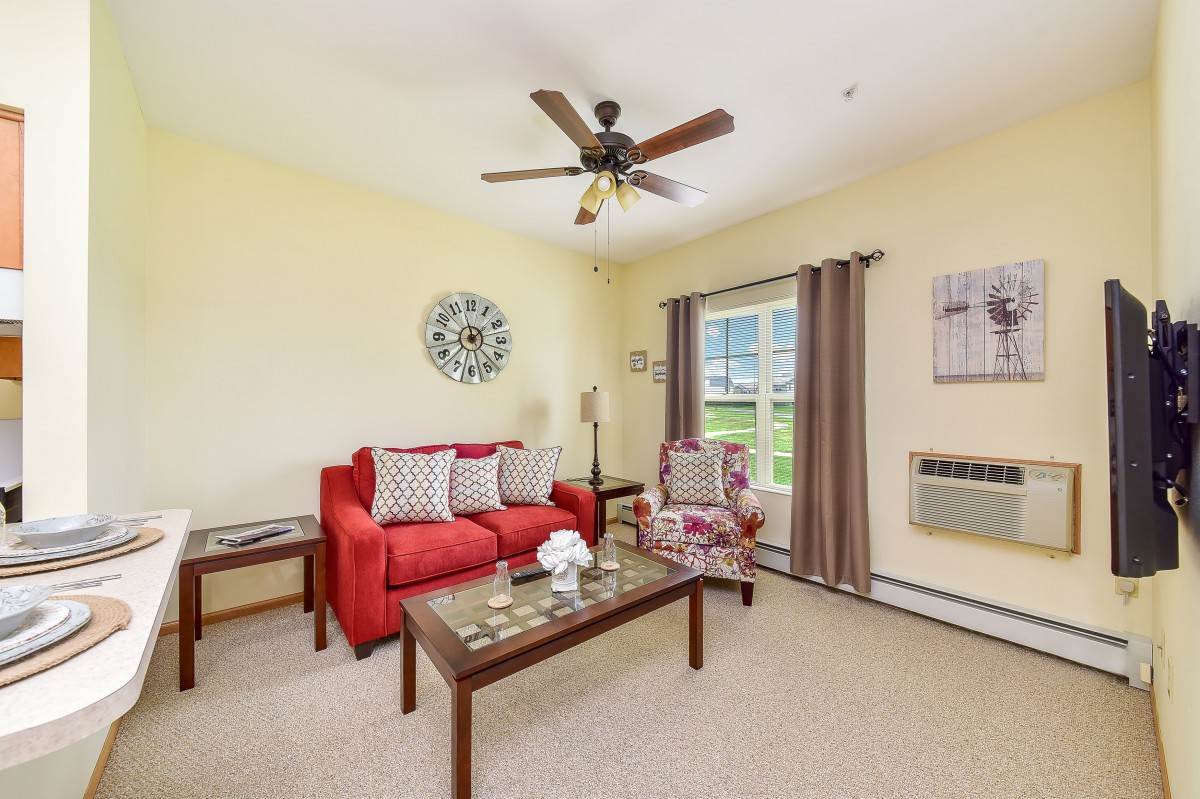 A cozy living room with a red sofa, armchair, and a coffee table beneath a ceiling fan.