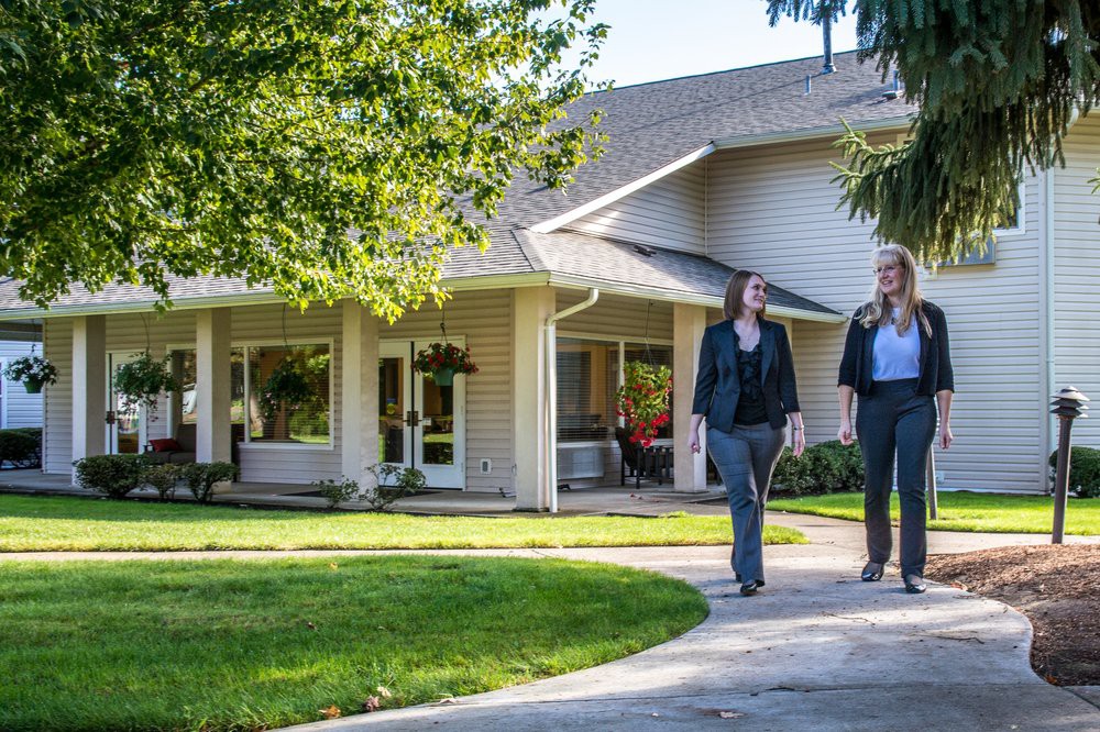 Two people walking on a pathway in front of a house surrounded by greenery.